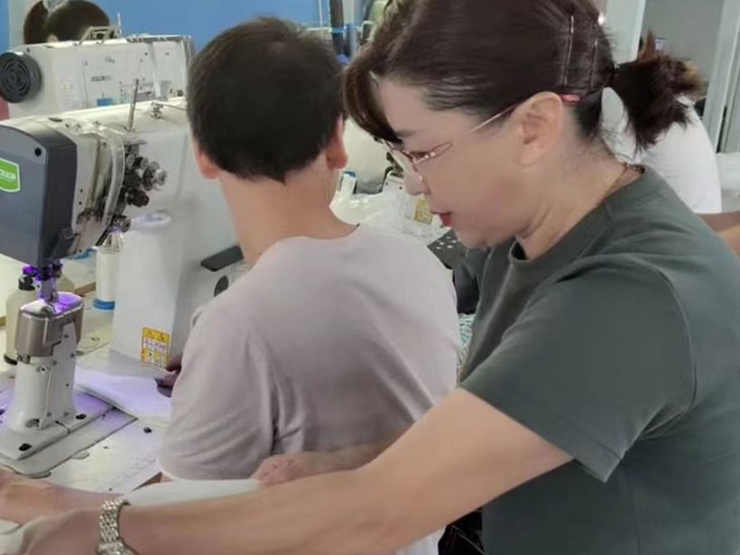 At one of our partner factories: a KicksCo team member guiding a machine operator at an industrial sewing machine.