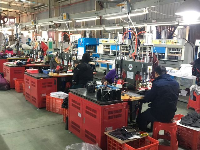 At one of our partner factories: workers at red workstations stitching and pressing shoe uppers on a factory floor.